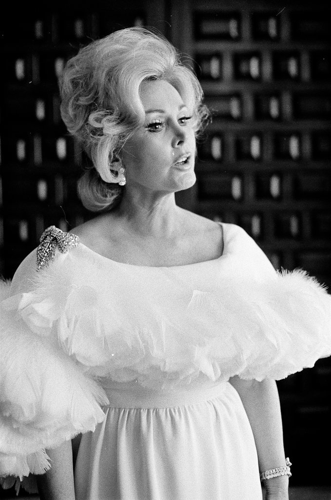 Zsa Zsa Gabor poses in a white dress in a hotel room - Fred Stein for Chicago Daily News