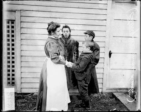 Cherry mine disaster, woman and three children facing each other, standing in a circle with their hands linked in front of a wooden building in Cherry, Illinois, after the St. Paul Coal Company mine fire - Chicago Daily News, Inc.