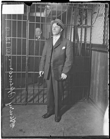 Henry Spencer, confessed murderer of Mrs. Mildred Allison Rexroat, standing in a jail cell with another man in the background behind the cell door - Chicago Daily News, Inc.