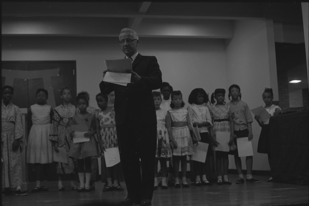 Man handing out certificates to children - Flerlage, Raeburn, 1915-2002