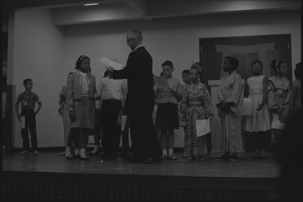 Man handing out certificates to children - Flerlage, Raeburn, 1915-2002