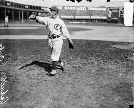 Baseball player Frank Wildfire Schultz of the Chicago Cubs standing on the field in a baseball stadium, extending his right arm out at shoulder height as if throwing a ball - Chicago Daily News, Inc.