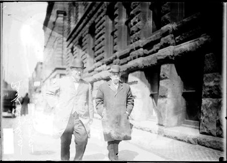 Buck Buchner, lawyer, walking with an unidentified man along a sidewalk next to the Criminal Courts Building - Chicago Daily News, Inc.