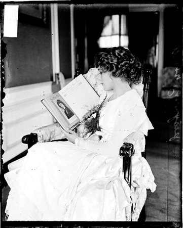 Silent film actress, Mary Pickford, sitting sideways in a chair, holding a book of portraits, her face turned slightly away from camera - Chicago Daily News, Inc.