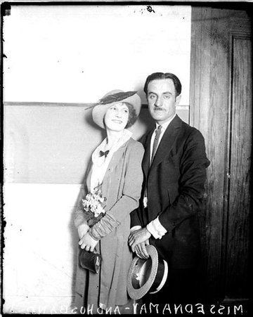 Edna May and her husband, Mr. Servert Grant, standing together and smiling in room - Chicago Daily News, Inc.