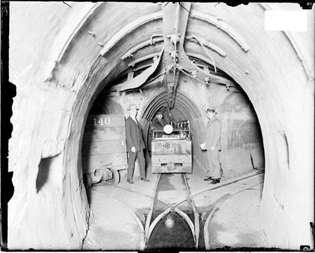 Two man standing in front of openings to three tunnels in Chicago freight tunnel network - Chicago Daily News, Inc.