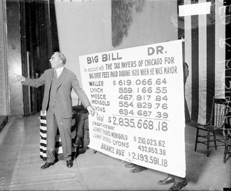 Attorney Edward Litsinger speaking and standing in front of a large poster documenting city finances on a stage in an auditorium - Chicago Daily News, Inc.