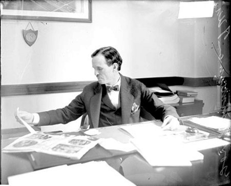 Governor Fred R. Zimmerman of Wisconsin sitting at a desk covered with papers, holding a piece of paper and looking to his right - Chicago Daily News, Inc.