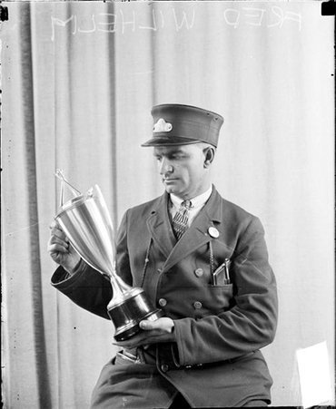 Fred Wilhelm of the Chicago Daily News looking at a trophy that he is holding, sitting in front of a light-colored backdrop in a room - Chicago Daily News, Inc.