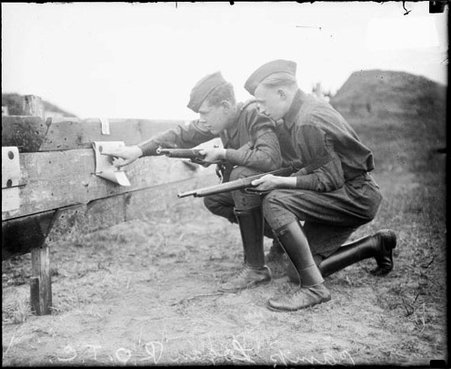 Reserve Officer Training Corps trainees holding rifles and kneeling behind a low wooden fence at a training facility - Chicago Daily News, Inc.