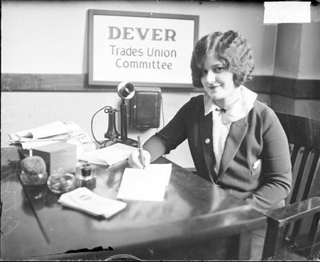 Esther Fenerson looking toward the camera, sitting at a table and writing on a pad of paper in a room - Chicago Daily News, Inc.