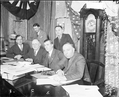 T. McCarthy, Thomas Burran, Frank Ryan, C. Baker, John Lee, and attorney Ben Goldstein sitting and standing at a table - Chicago Daily News, Inc.