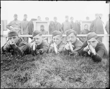 Reserve Officer Training Corps trainees facing the camera, aiming rifles from behind a grass embankment, lighter exposure - Chicago Daily News, Inc.