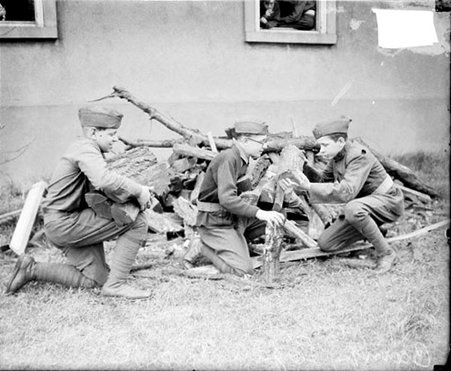 Reserve Officer Training Corps trainees kneeling by a pile of wood and holding logs at a training facility - Chicago Daily News, Inc.