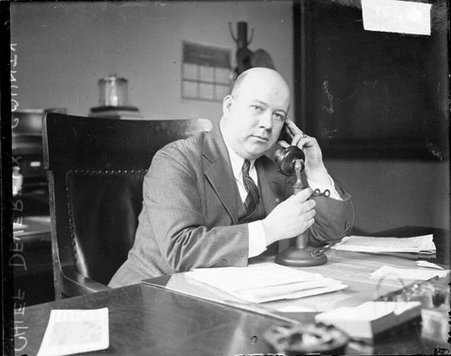 Police Chief of Devereux County looking at camera, holding telephone earpiece to his ear and holding the receiver with his right hand - Chicago Daily News, Inc.