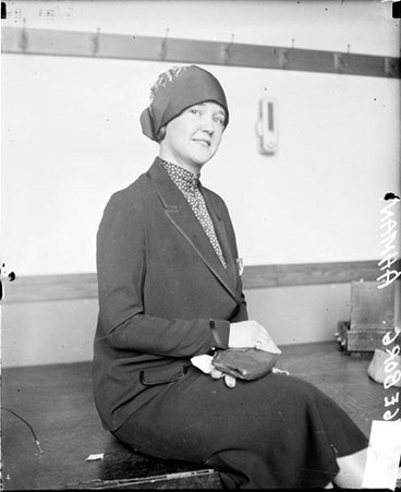 Ingeborg Ahmans looking toward the camera and tilting her head to the left, sitting on a table in front of a light-colored wall in a room - Chicago Daily News, Inc.