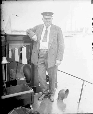 G. W. Bradley looking to his left while standing on the deck of a boat moored in a harbor - Chicago Daily News, Inc.