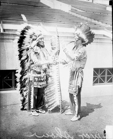 Two men shaking hands and wearing traditional Native American headdresses and clothing at a military tournament at Soldier Field - Chicago Daily News, Inc.