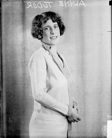 Alyne Tudor looking toward the camera and standing in front of a light-colored backdrop - Chicago Daily News, Inc.