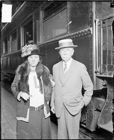 Mr. and Mrs. Edward L. Doheny looking toward the camera, standing in front of a passenger train car in a train station - Chicago Daily News, Inc.