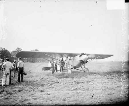 Aviator Thomas P. Nelson and two unidentified men standing next to a propeller airplane on an airfield - Chicago Daily News, Inc.