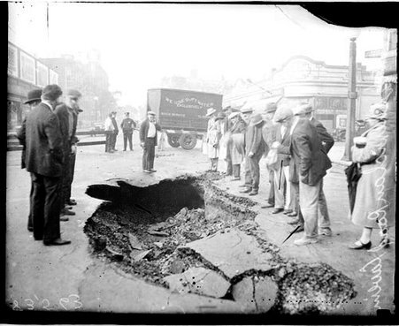 Crowd standing around a portion of Sheridan Road where the street has caved in - Chicago Daily News, Inc.
