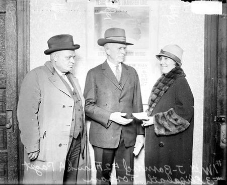 William J. Barnard, Elizabeth Forham, and Frank A. Paget standing and facing each other in a room - Chicago Daily News, Inc.