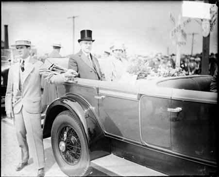 President Calvin Coolidge looking toward the camera, sitting with his wife in the backseat of a convertible automobile on a road in Indiana - Chicago Daily News, Inc.