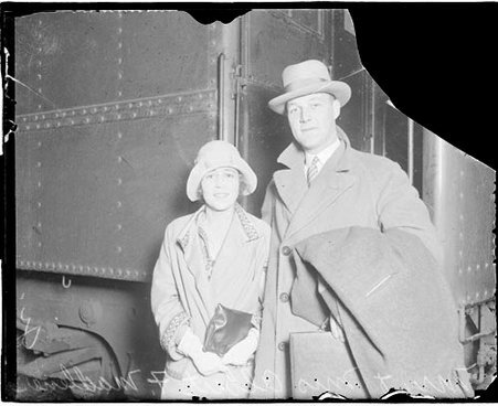 Mr. and Mrs. Albert Madlener looking toward the camera and standing in front of a passenger train car - Chicago Daily News, Inc.