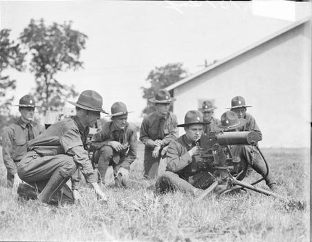 Group of soldiers sitting and kneeling behind a machine gun on a field - Chicago Daily News, Inc.