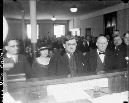 Benedict Short standing in front of a long podium in a courtroom, people standing and sitting around him - Chicago Daily News, Inc.