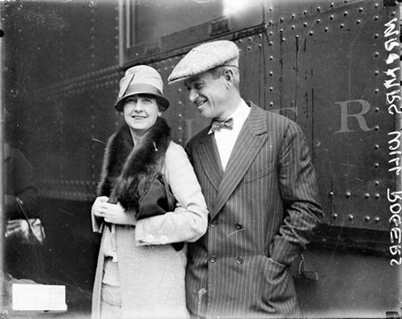 Will Rogers and his wife Betty Blake Rogers standing in front of a passenger train car in a train station - Chicago Daily News, Inc.