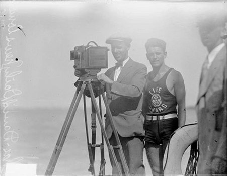 Chicago Daily News cameraman standing next to a lifeguard on a beach - Chicago Daily News, Inc.