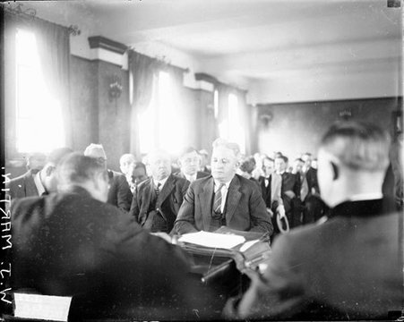 W. J. Martin looking down, sitting at a table in a crowded courtroom, dark exposure - Chicago Daily News, Inc.