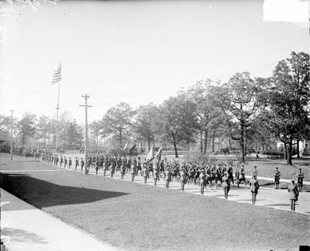 Regiment of soldiers carrying rifles marching on a street, soldiers standing at attention lining the street - Chicago Daily News, Inc.