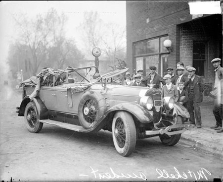 Group of men and boys standing on the sidewalk next to the wrecked automobile of John J. Mitchell - Chicago Daily News, Inc.