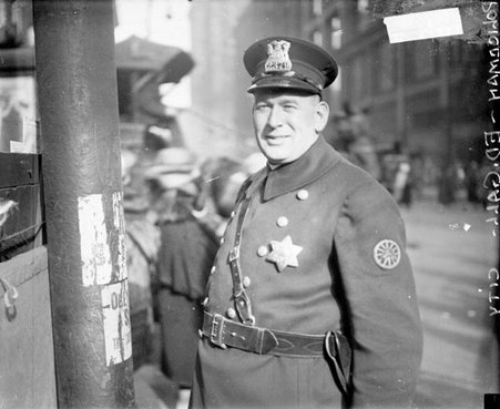 Police officer Edward Gall looking toward the camera, standing next to a pole on a sidewalk - Chicago Daily News, Inc.
