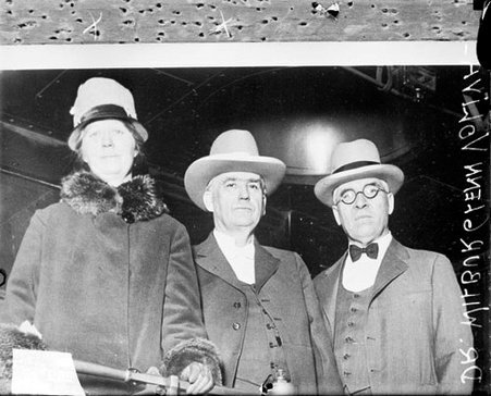Dr. Wilbur Glenn Voliva standing with a man and a woman on the rear platform of a passenger train car - Chicago Daily News, Inc.