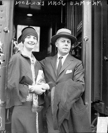 Mr. and Mrs. John Borden looking toward the camera, standing on the steps of a passenger train car in a railroad station - Chicago Daily News, Inc.