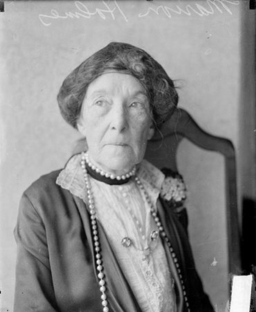 Marion Holmes looking to her right, sitting in front of a backdrop in a room, dark exposure - Chicago Daily News, Inc.