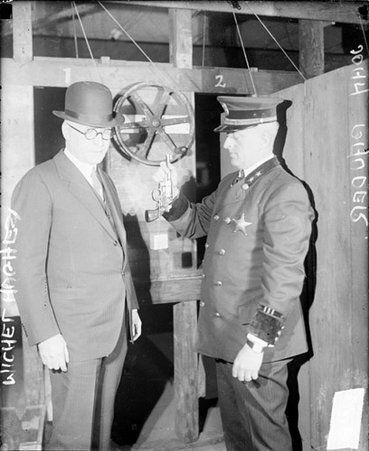 Police officer John Bauder holding a pistol by the barrel, standing with Michael Hughes in a room - Chicago Daily News, Inc.