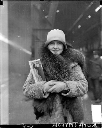 Ruth Taylor looking toward the camera, standing on a train platform in a train station - Chicago Daily News, Inc.