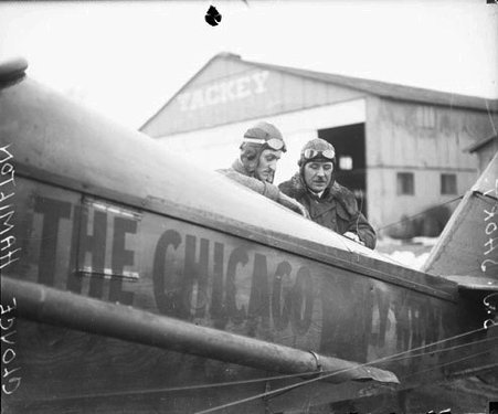 Shirley J. Short and Cloyce Hamilton wearing flight headgear and goggles, standing behind a two-person airplane, dark exposure - Chicago Daily News, Inc.