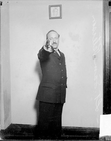 Detective Samuel Peterson aiming a pistol toward the camera, standing in a room - Chicago Daily News, Inc.