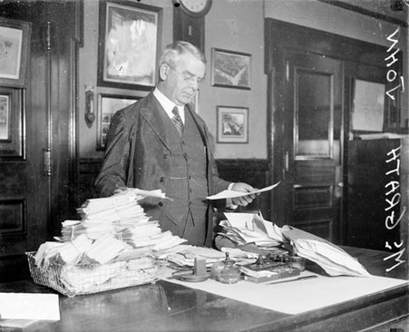 John T. McGrath standing at a desk in a room covered with stacks of mail - Chicago Daily News, Inc.