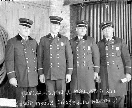 Four fire department officers in uniform looking toward the camera, standing in a room - Chicago Daily News, Inc.