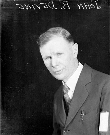 John B. Devine looking toward the camera, sitting in front of a backdrop in a room - Chicago Daily News, Inc.