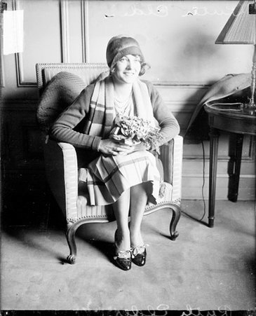 Pilot Ruth Elder looking to the right of the camera, holding a floral arrangement, sitting in a room - Chicago Daily News, Inc.