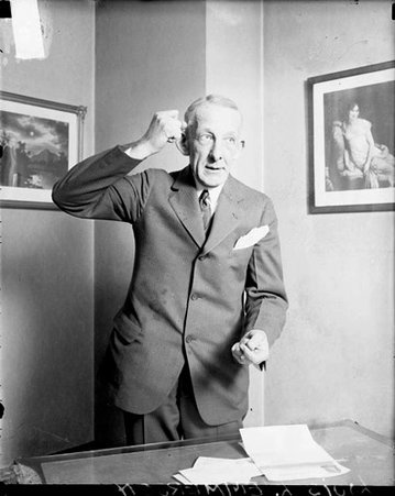 Louis L. Emmerson clenching his hands into fists, standing behind a desk in a room - Chicago Daily News, Inc.