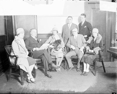 Four men and three women sitting and standing in a room, light exposure - Chicago Daily News, Inc.